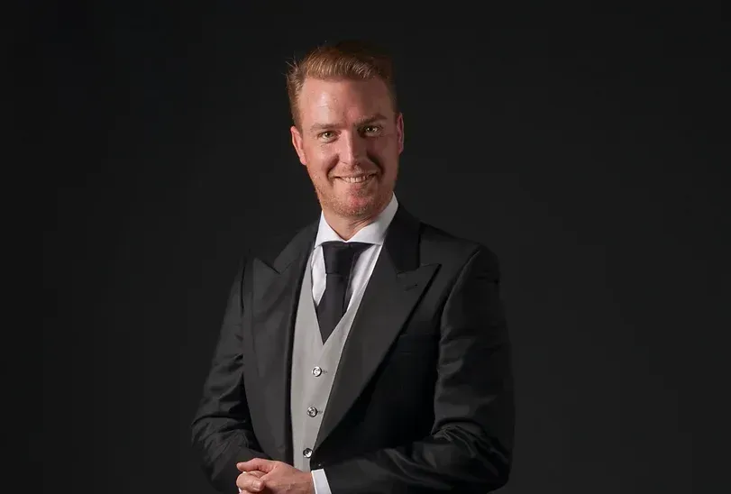 Een man in smoking en stropdas lacht naar de camera.