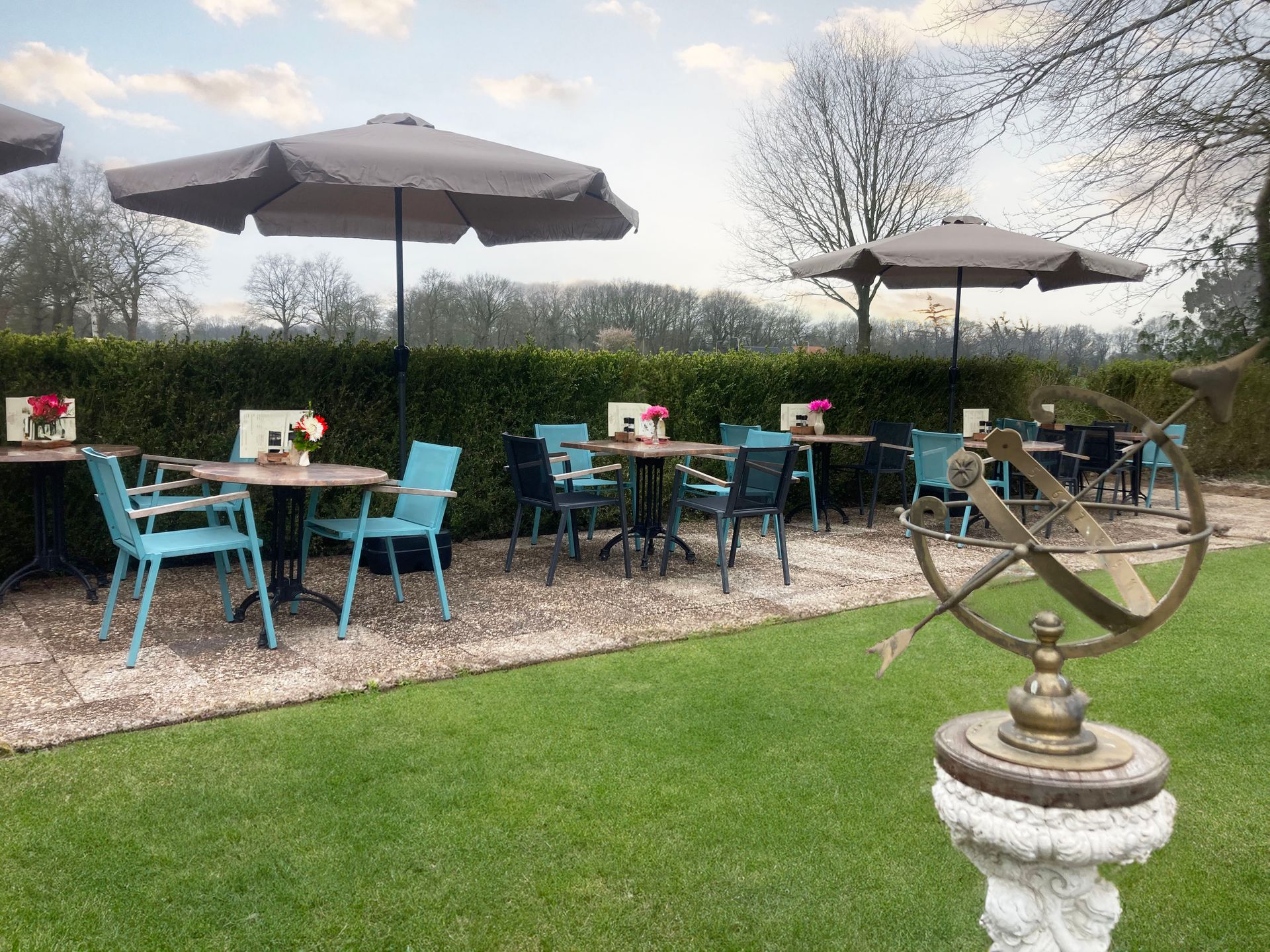 Een terras met tafels, stoelen, parasols en een zonnewijzer.