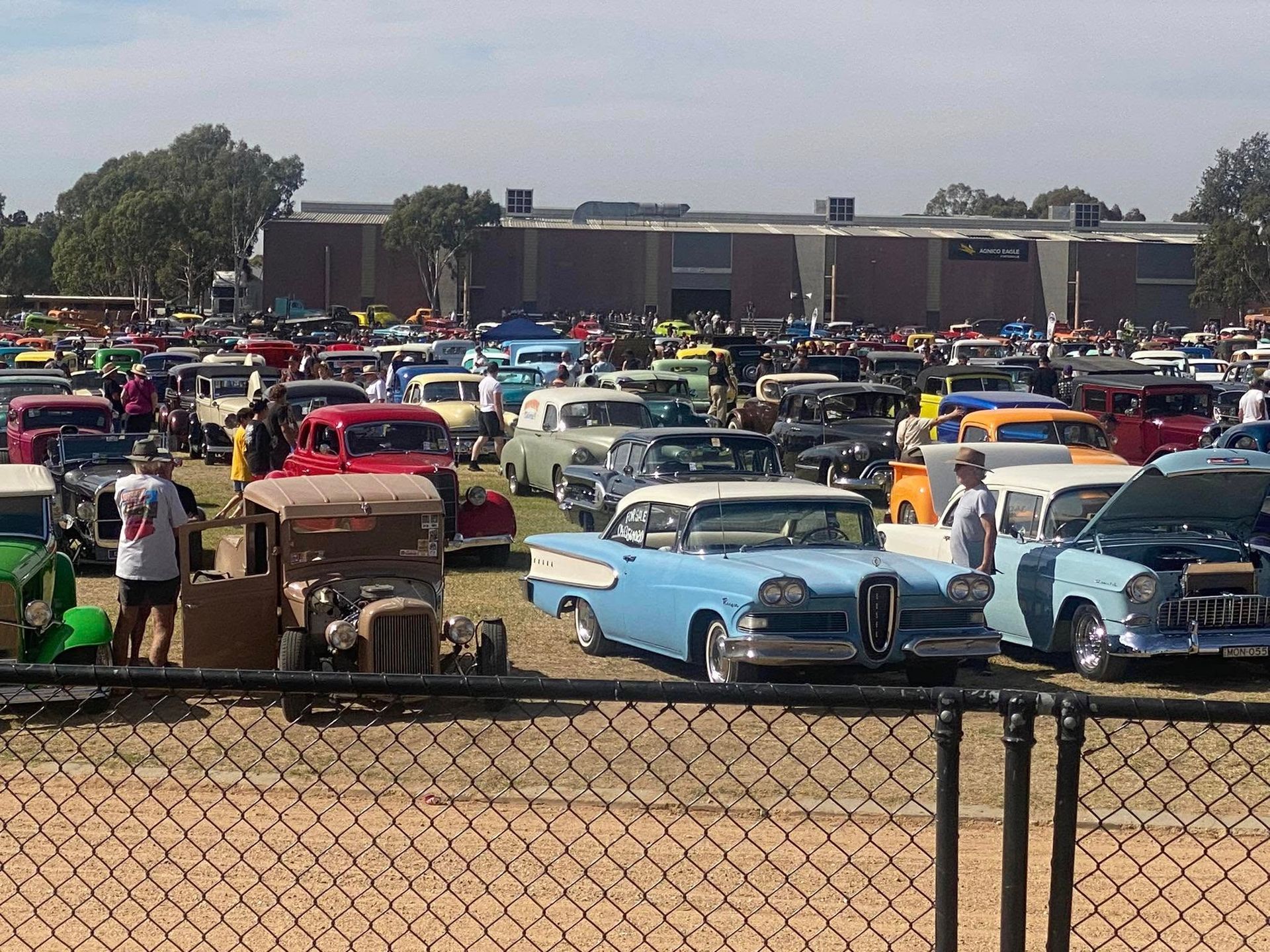 lots of cars parked in a grid formation in a paddock surrounded by a black chain fence 