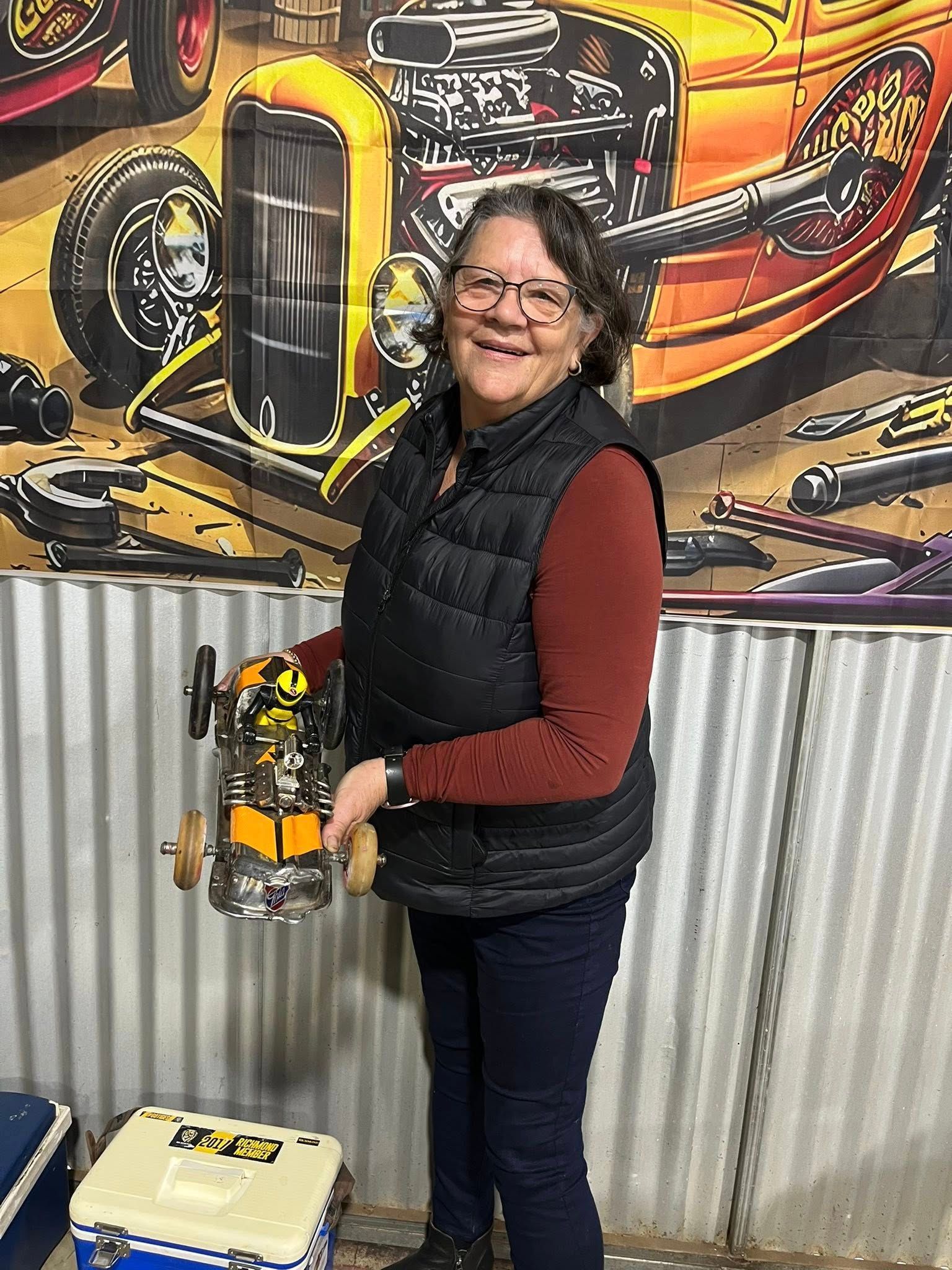 Woman standing in front of tin shed holding a small car 