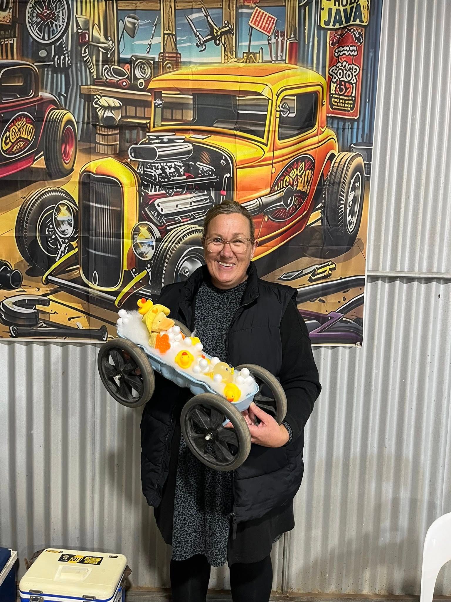 Woman standing in front of tin shed holding a small car 