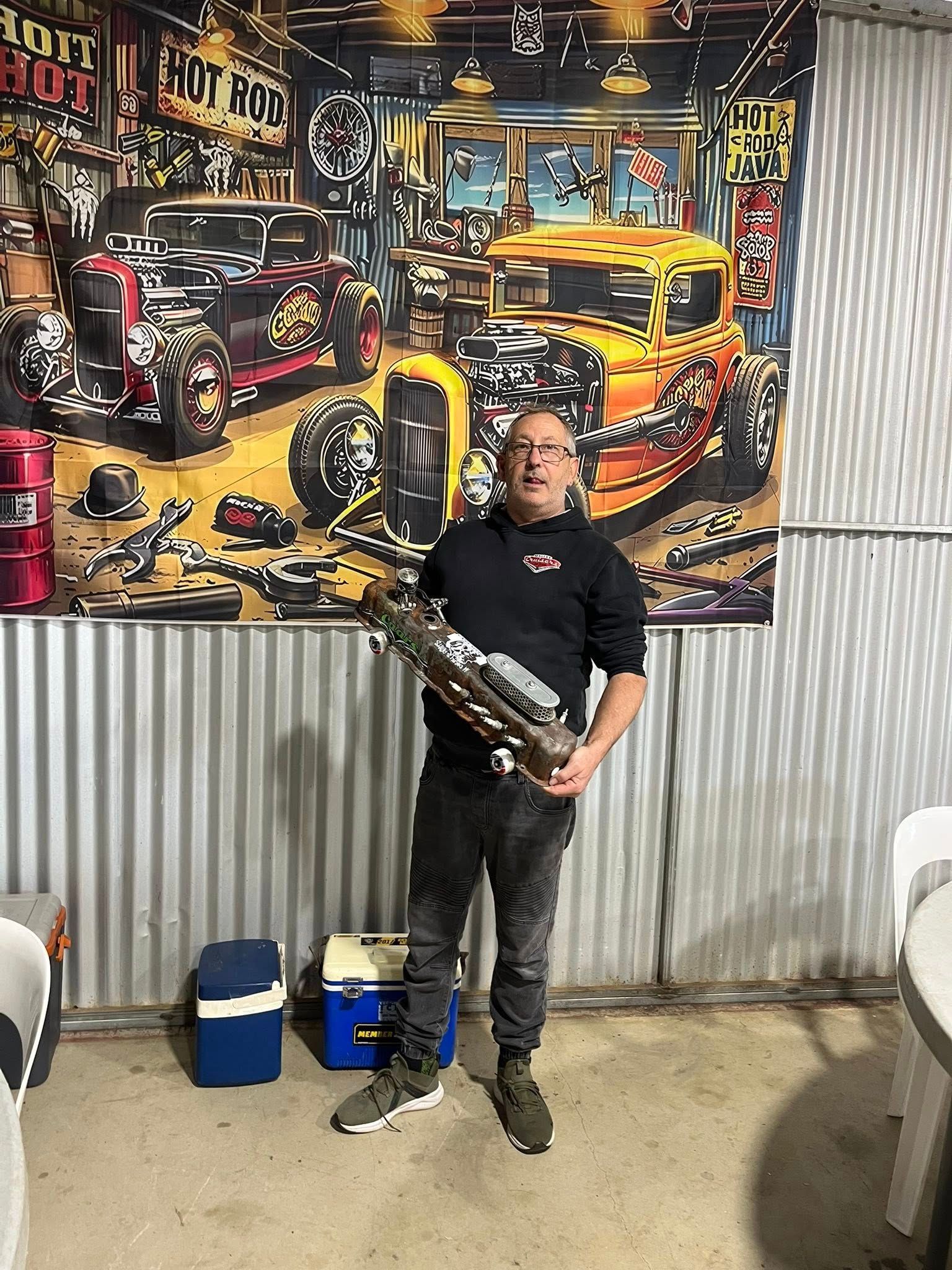 Man standing in front of tin shed holding a small car 