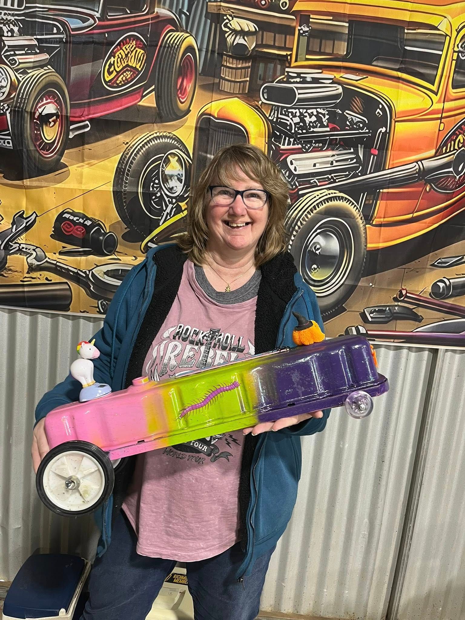 Woman standing in front of tin shed holding a small car 
