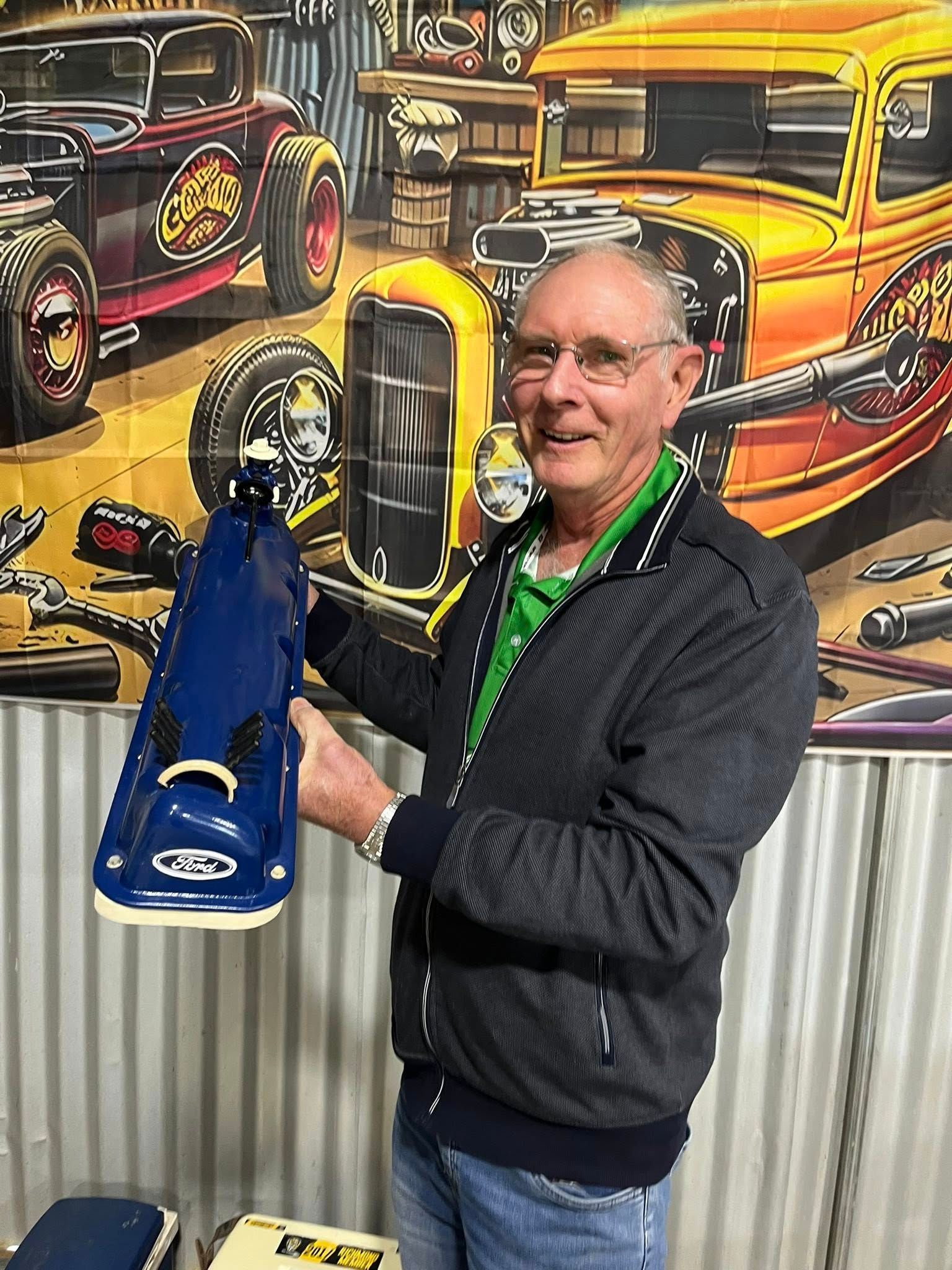 Man standing in front of tin shed holding a small car 