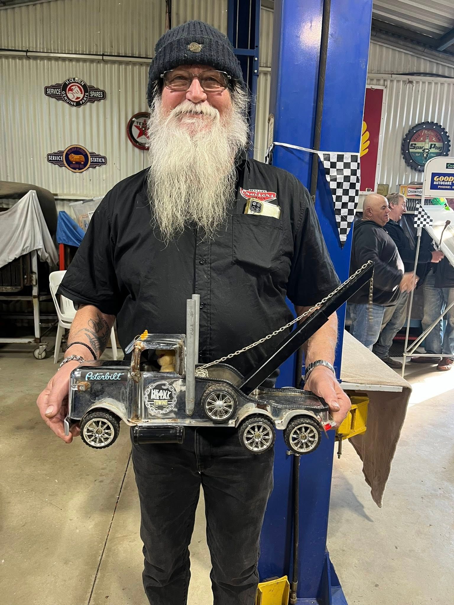 Man standing in front of tin shed holding a small car 