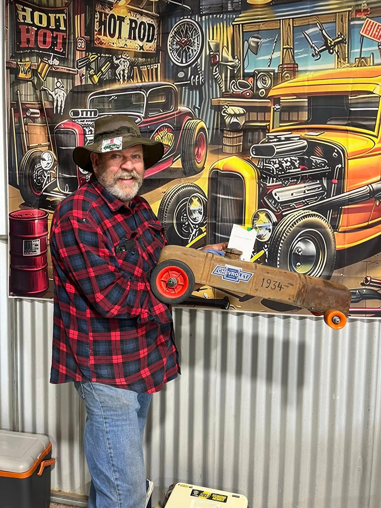 Man standing in front of tin shed holding a small car 