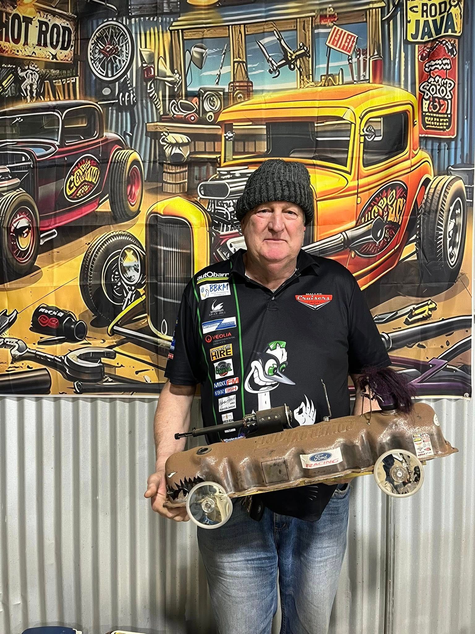 Man standing in front of tin shed holding a small car 