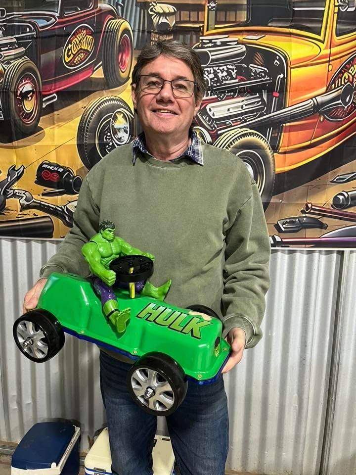Man standing in front of tin shed holding a small car 
