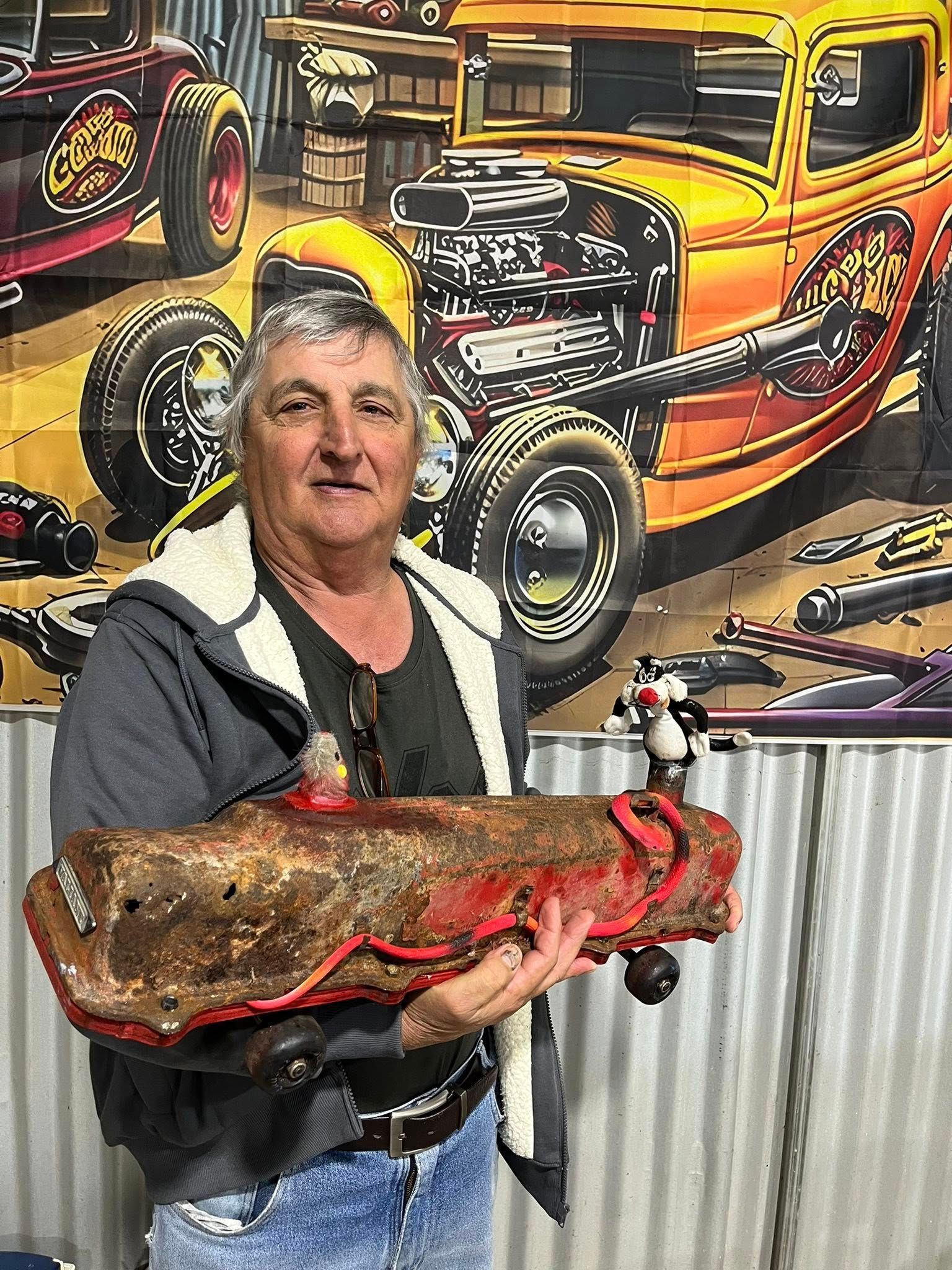 Man standing in front of tin shed holding a small car 