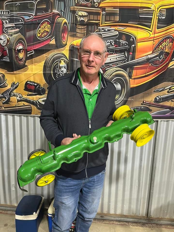 Man standing in front of tin shed holding a small car 