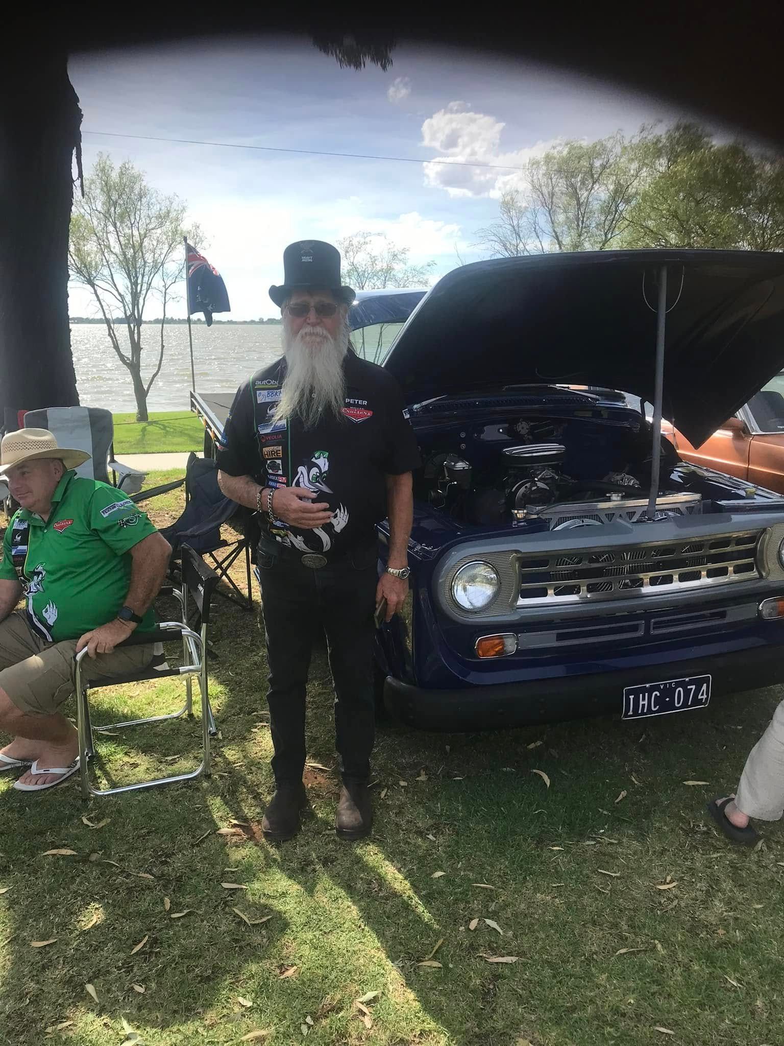 man wearing a top hat stands in front of his car
