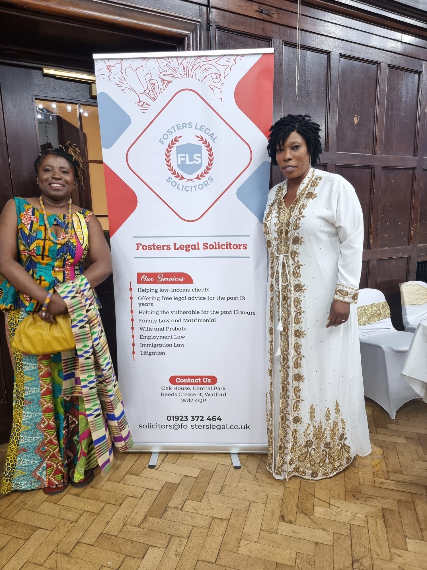 Two women in formal attire pose by a banner for