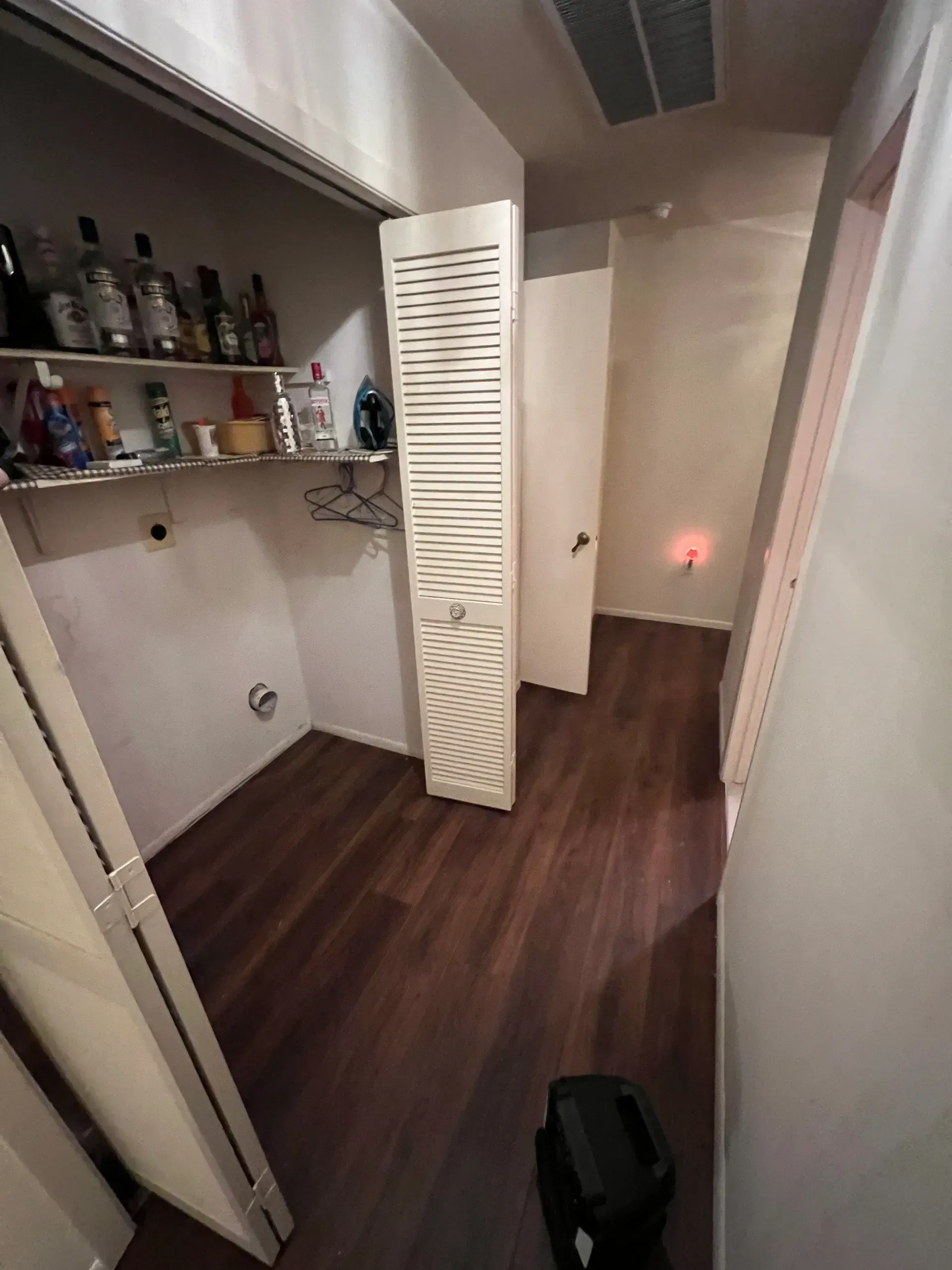 A walk in closet with wooden floors and shelves filled with bottles.