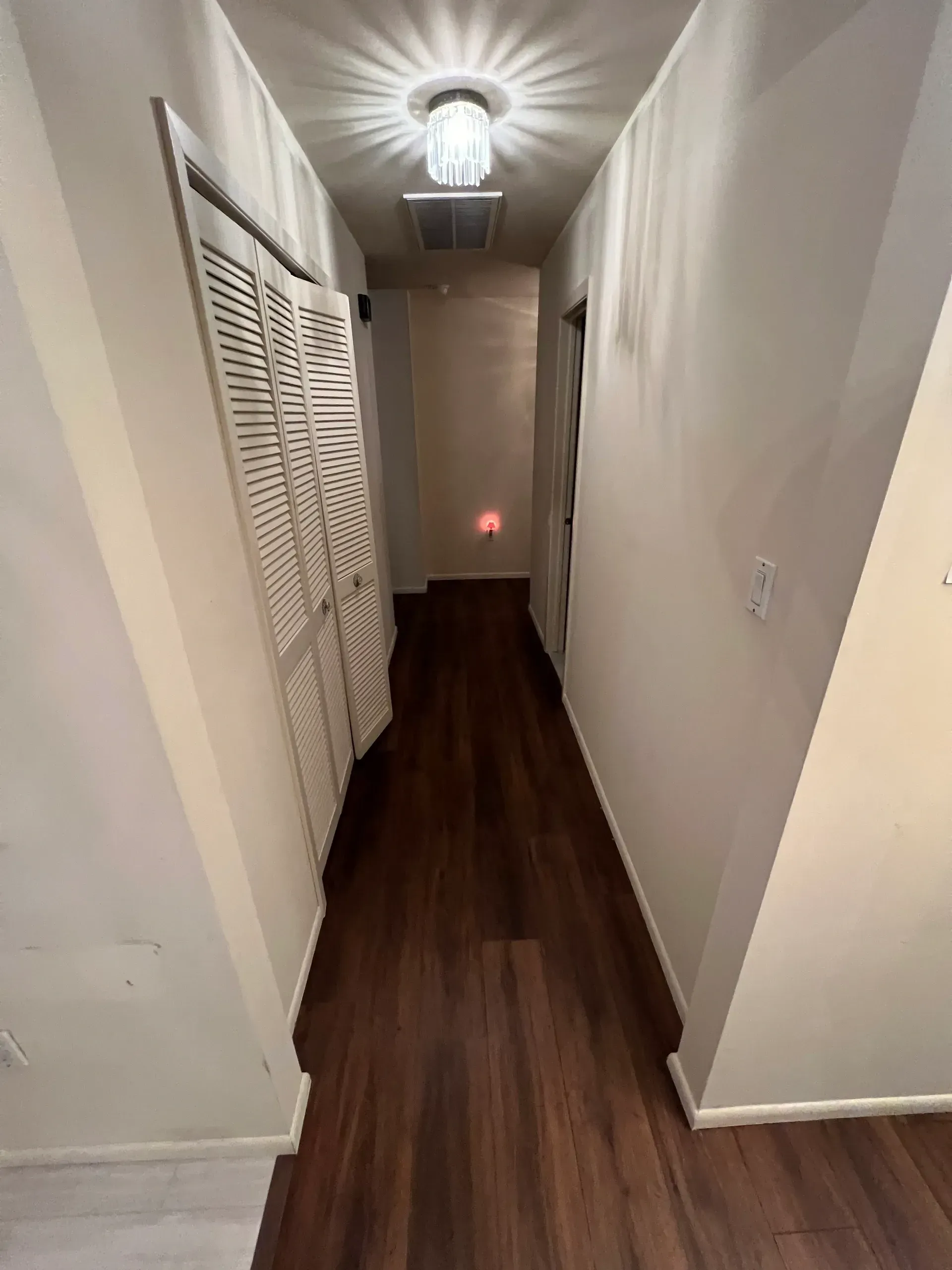 A long hallway with hardwood floors and a light on the ceiling.