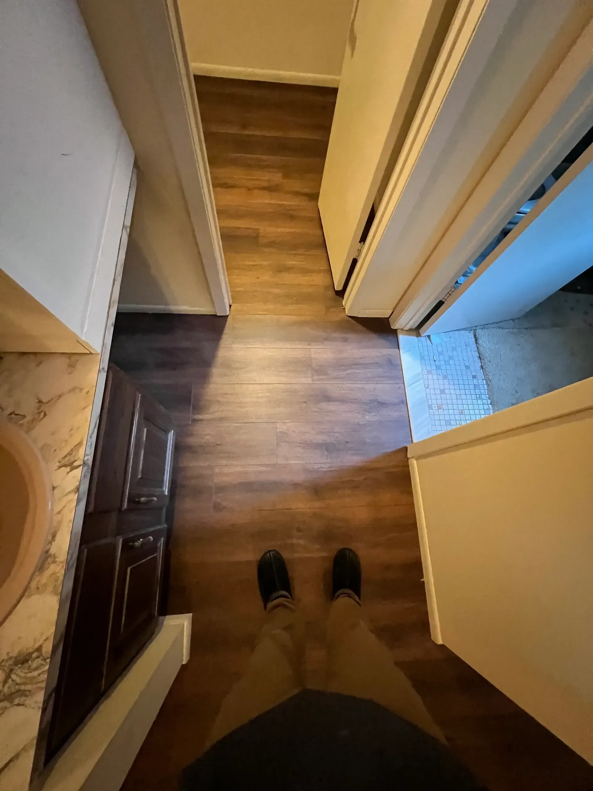 A person is standing on a wooden floor in a hallway.