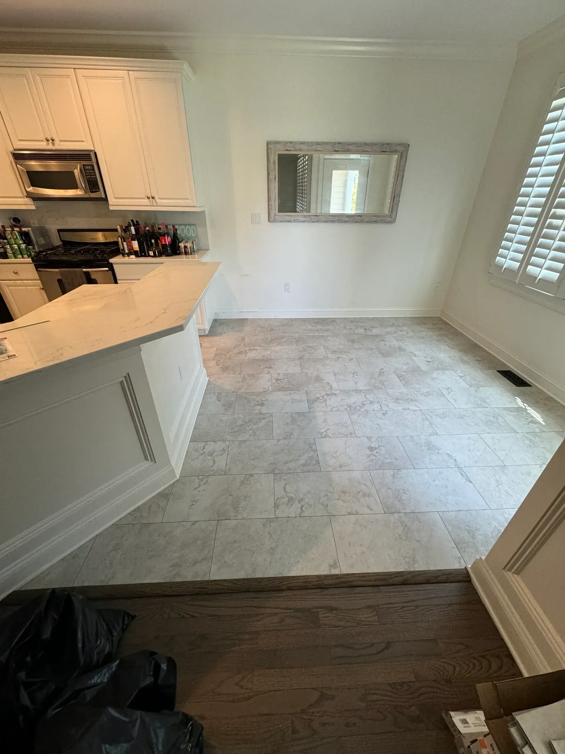 A kitchen with white cabinets and hardwood floors and a mirror on the wall.