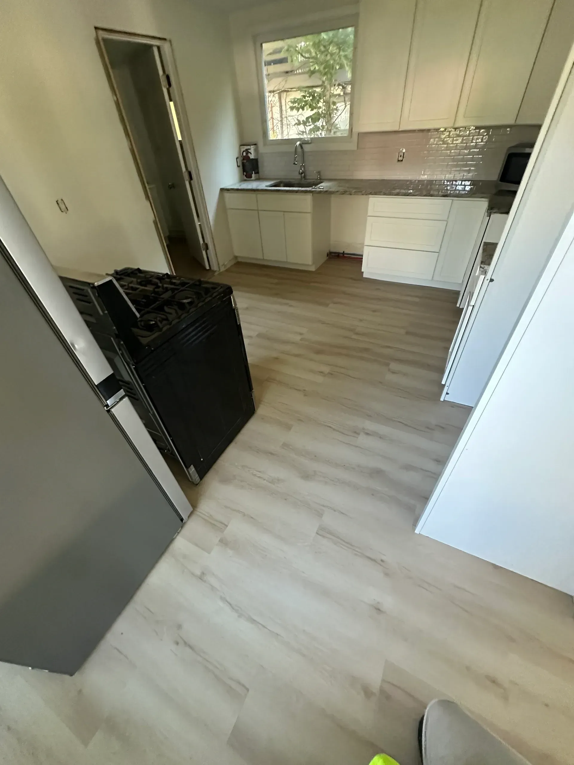 A kitchen with hardwood floors , white cabinets , a stove and a refrigerator.