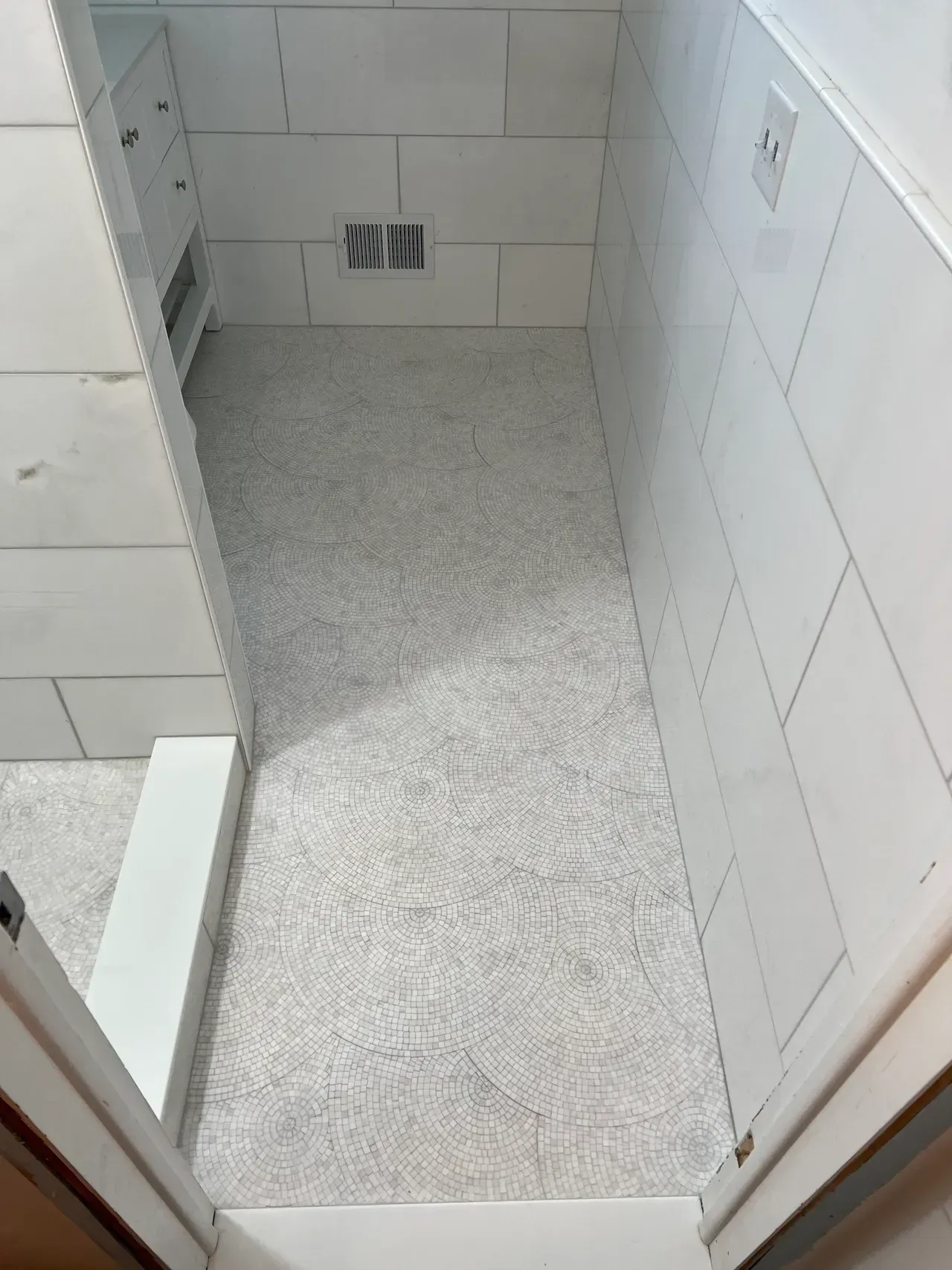 A bathroom with white tiles and a drain on the floor