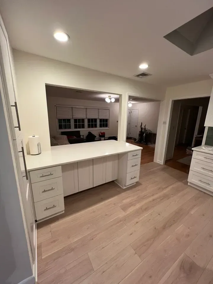A kitchen with white cabinets and a desk in the middle of the room.