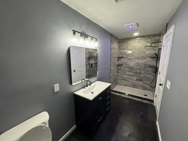 A bathroom with a sink , toilet , mirror and walk in shower.