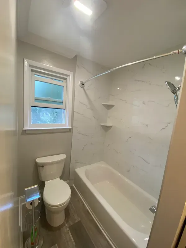 A bathroom with a toilet , tub , shower and window.