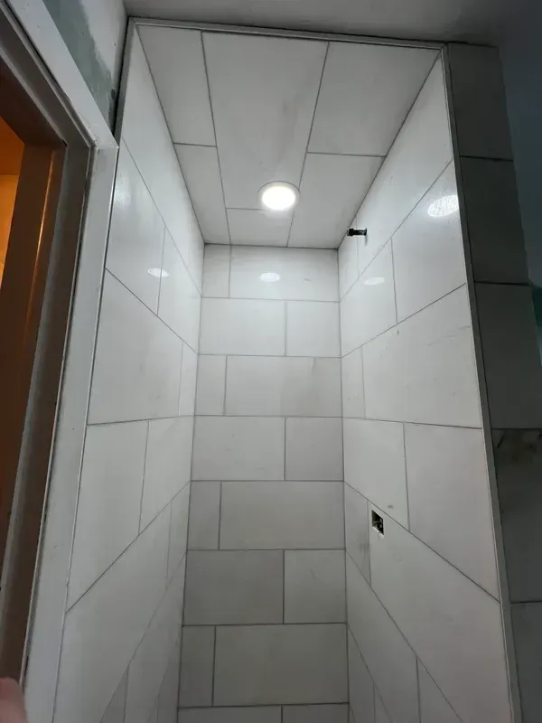 A bathroom with white tiles and a light on the ceiling.