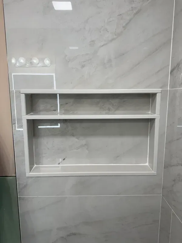 There is a shelf in the wall of a bathroom.