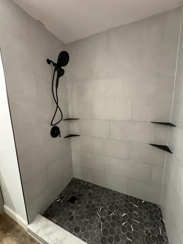 A shower with a black shower head and shelves in a bathroom.