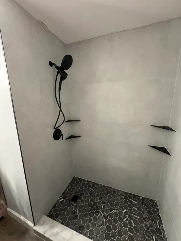 A shower with a shower head and shelves in a bathroom.