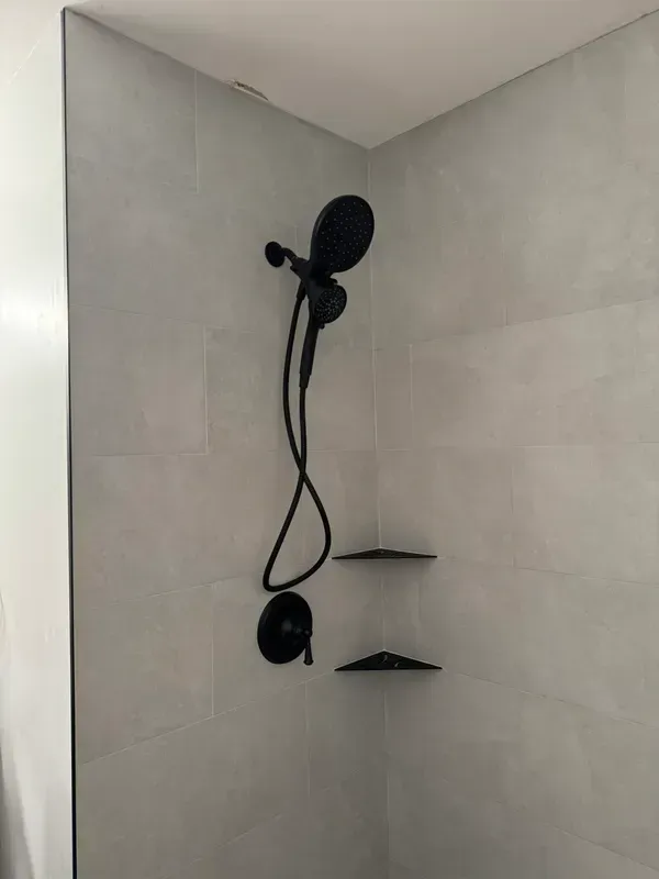 A shower with a black shower head and shelves.