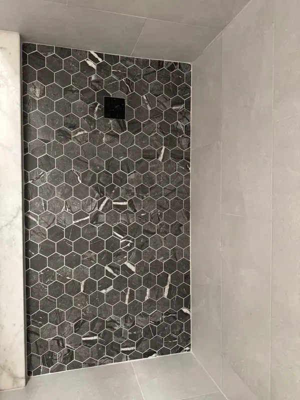 A shower stall with a black and white tile wall.