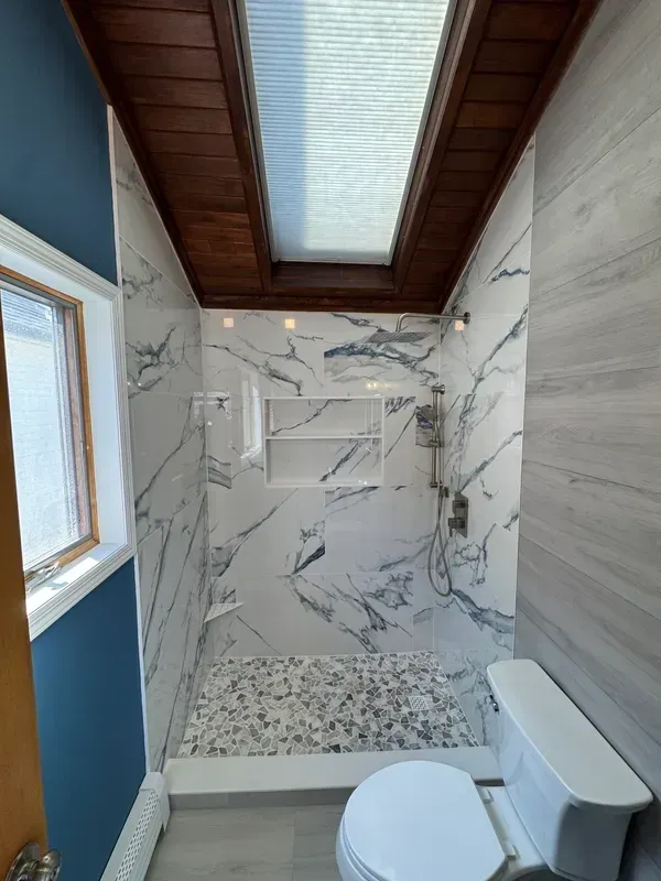 A bathroom with a toilet , shower , and skylight.