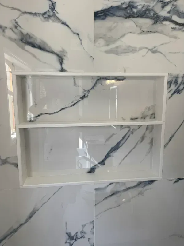 A bathroom with a marble wall and a shelf in the shower.