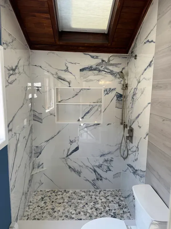 A bathroom with a toilet , shower , and skylight.