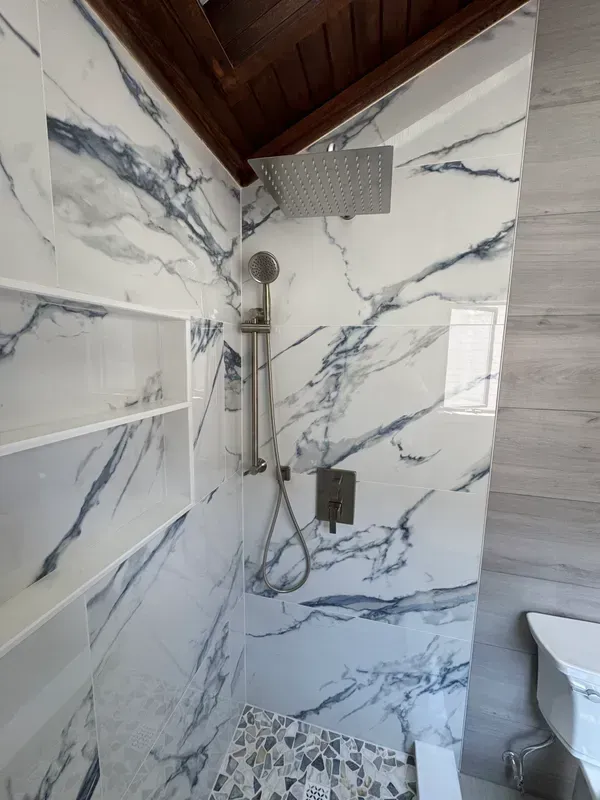A bathroom with marble walls , a toilet , and a shower.