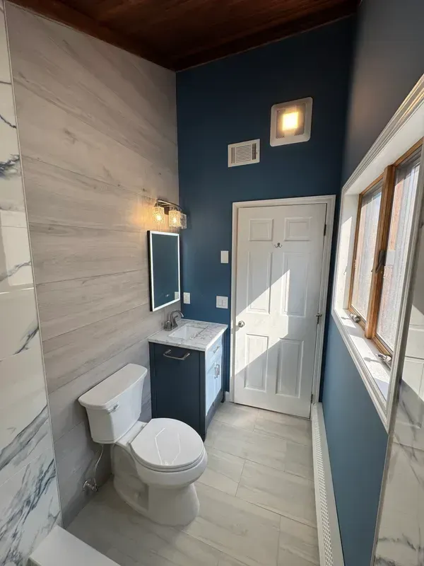 A bathroom with a toilet , sink and mirror.