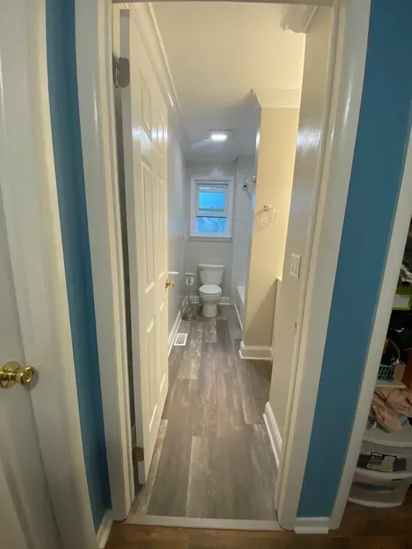 A hallway leading to a bathroom with a toilet and a window.