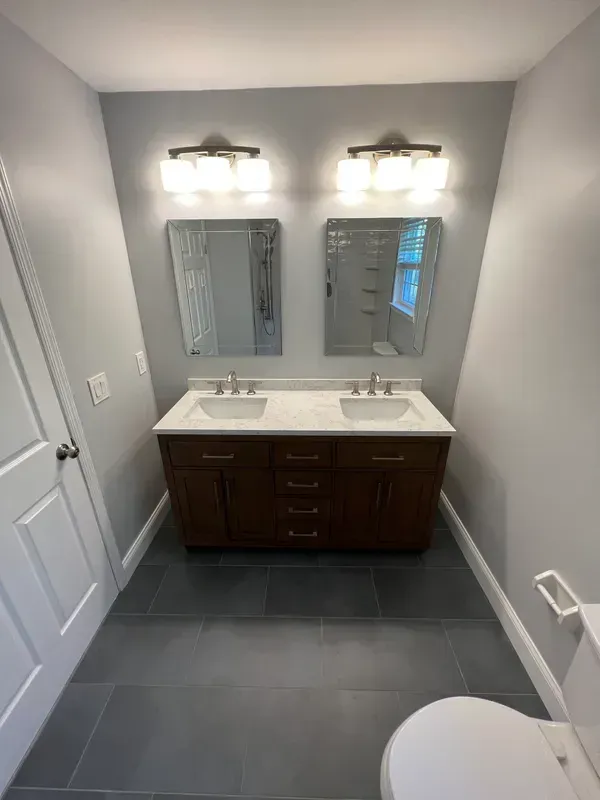 A bathroom with two sinks , two mirrors and a toilet.