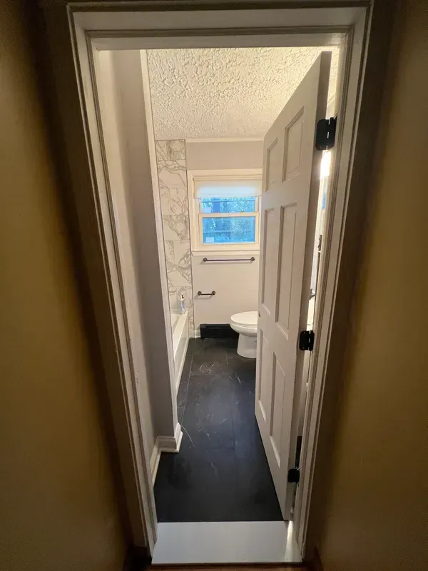 A bathroom with a toilet , bathtub , and window.