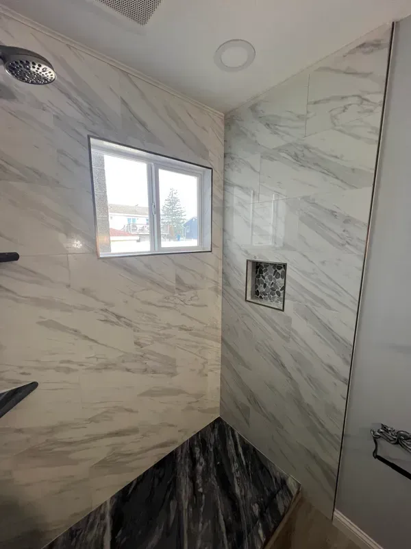 A shower with marble walls and a window.