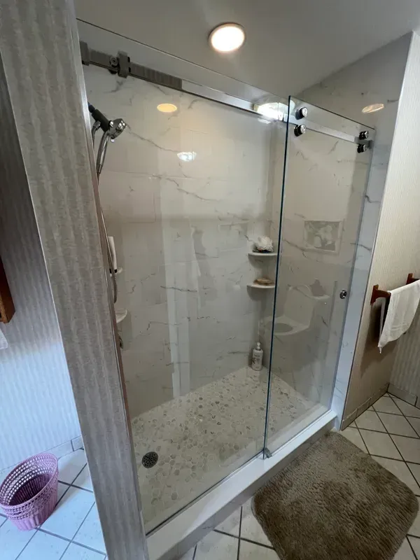 A bathroom with a walk in shower with a sliding glass door.