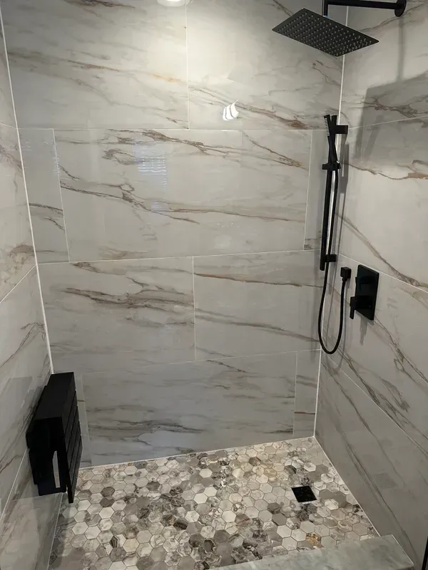 A walk in shower with marble tiles and a black shower head.