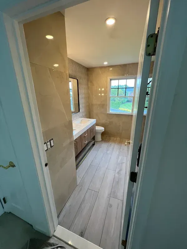 A bathroom with a sink , toilet , mirror and window.