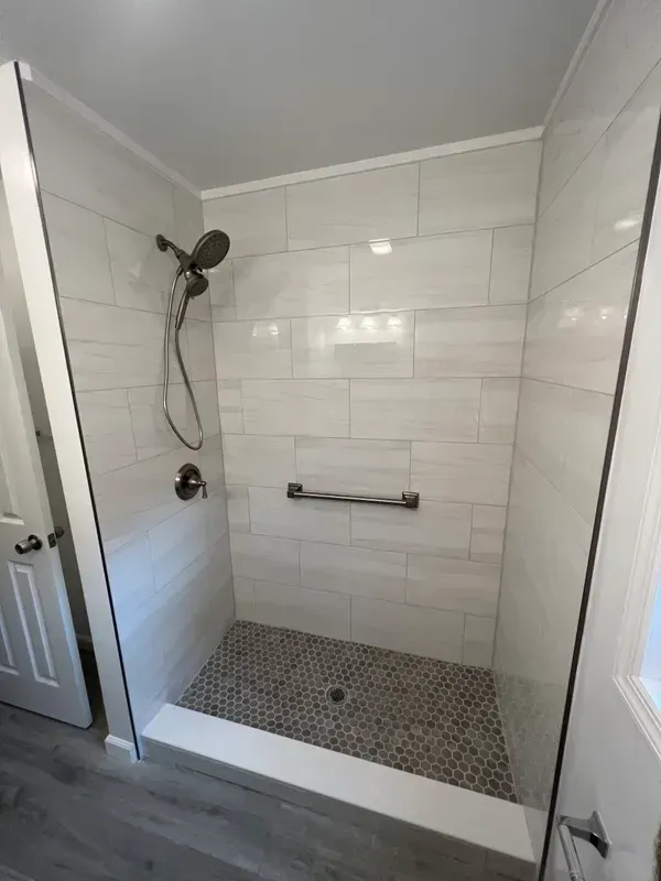 A walk in shower with a glass door and a hand rail.