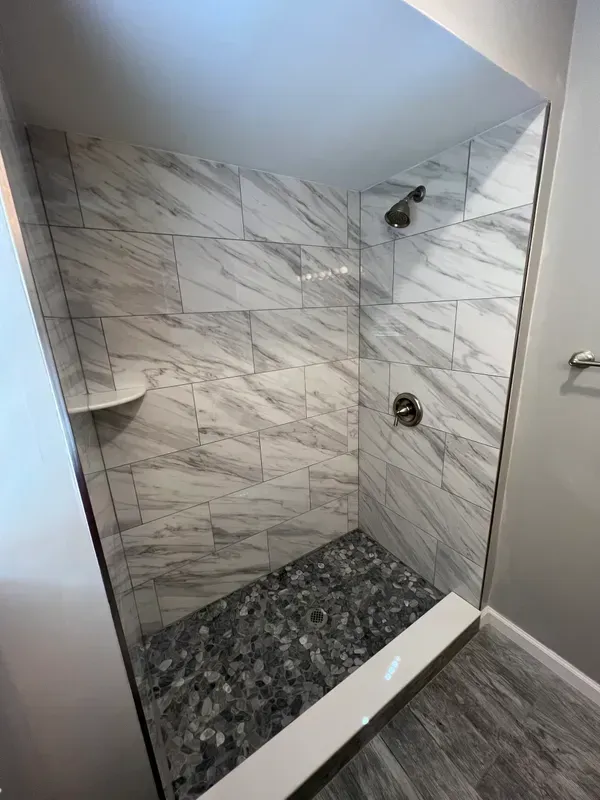 A bathroom with a walk in shower with marble tiles and a glass door.