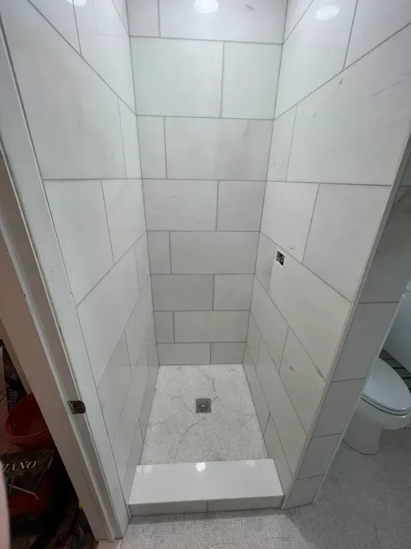 A bathroom with white tiles and a walk in shower.