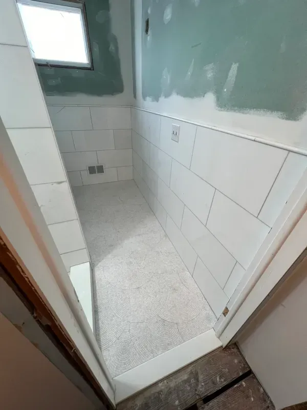 A bathroom under construction with white tiles and a window.