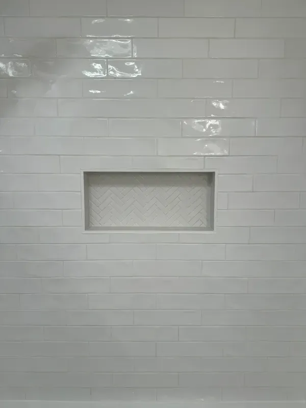 A white tiled wall with a niche in the middle of it.
