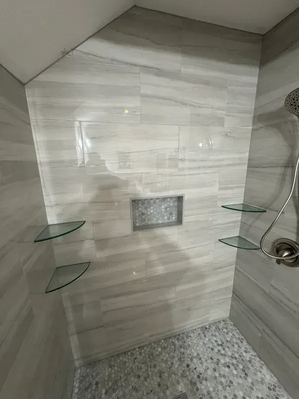 A shower with a glass shelf and a shower head.