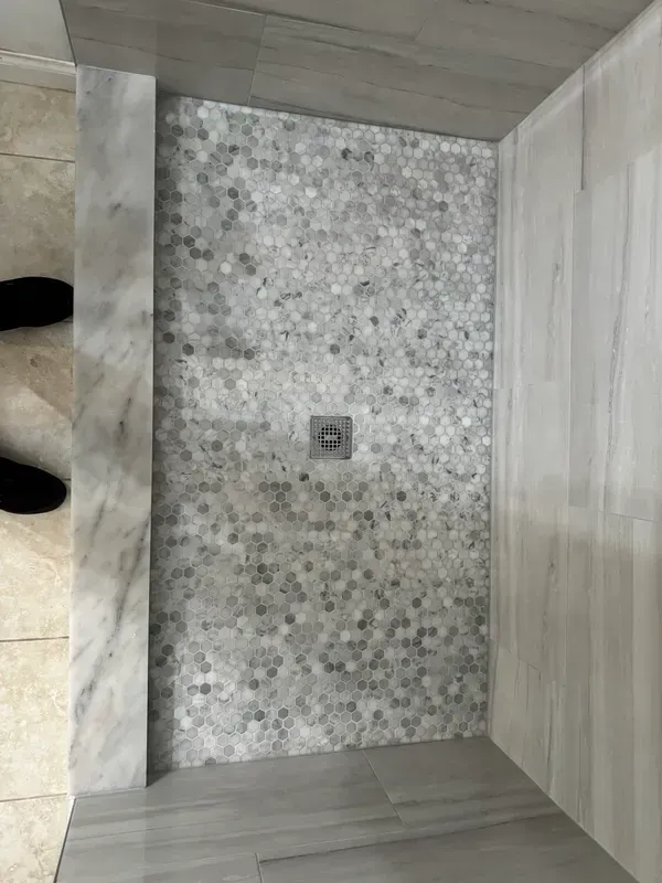 A person is standing in a shower with a tiled floor.